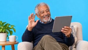 An older man enjoys a video conversation on a tablet against a bright blue background.